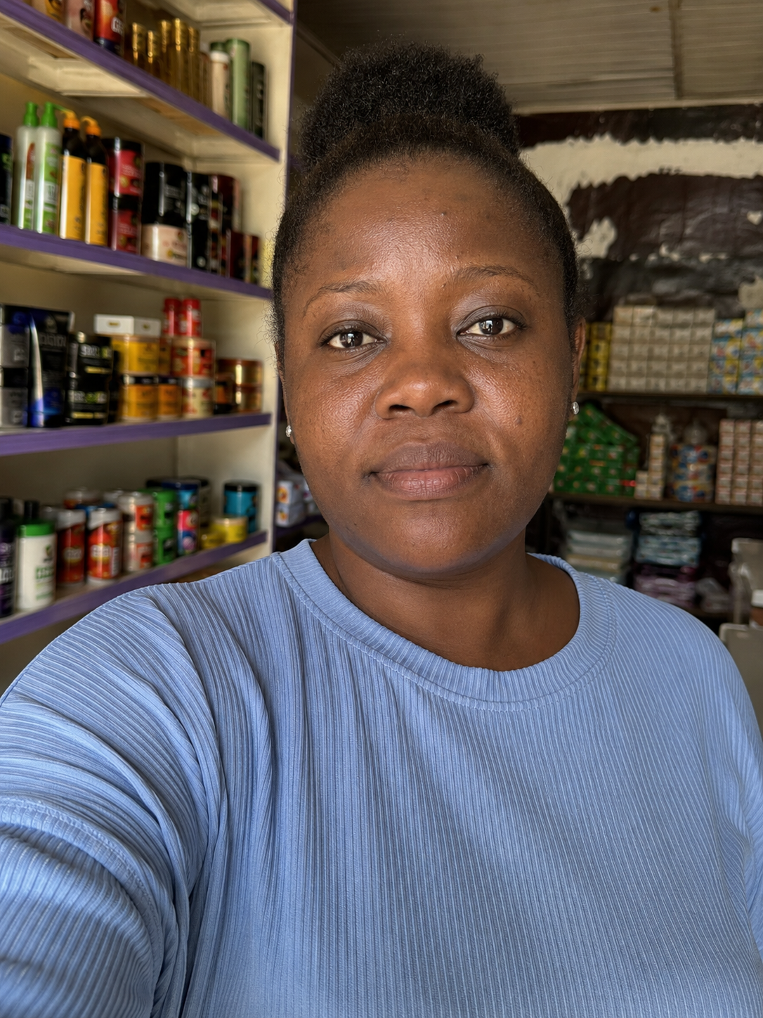 Efua, a small business owner, standing in her shop among stocked shelves
