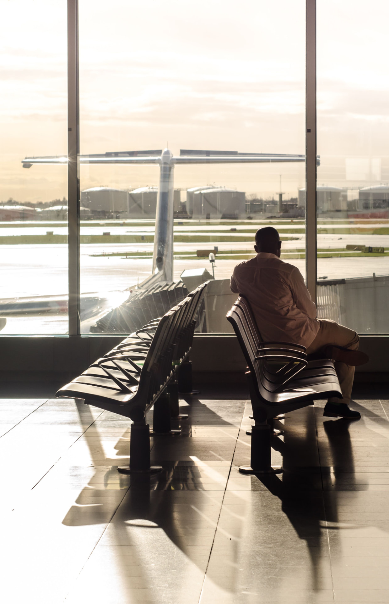 A traveller sitting in an airport departure lounge, looking out through the window at a plane on the tarmac